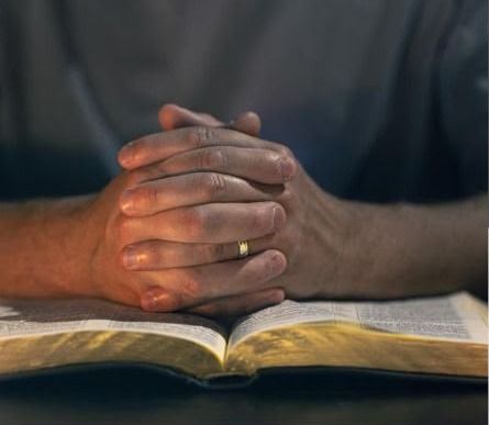 Hands folded in prayer on an open Bible